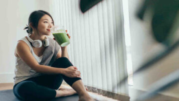 Beautiful young Asian woman in sportswear drinking protein shake after exercise, relaxing at home.