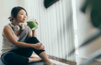 Beautiful young Asian woman in sportswear drinking protein shake after exercise, relaxing at home.