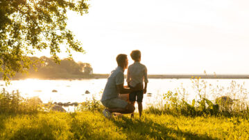 Father and his little son. Happy loving family walking outdoor in the light of sunset. Sea and field background