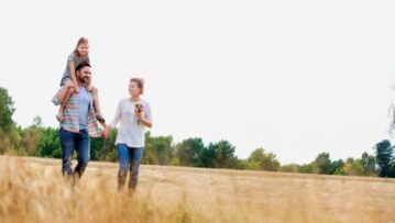 Young Caucasian family walking across field with young child on her fathers shoulders with the wife holding a bouquet of flowers