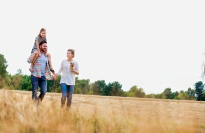 Young Caucasian family walking across field with young child on her fathers shoulders with the wife holding a bouquet of flowers