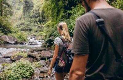 Rear view shot of young man and woman hiking in forest. Tourist couple walking by stream.